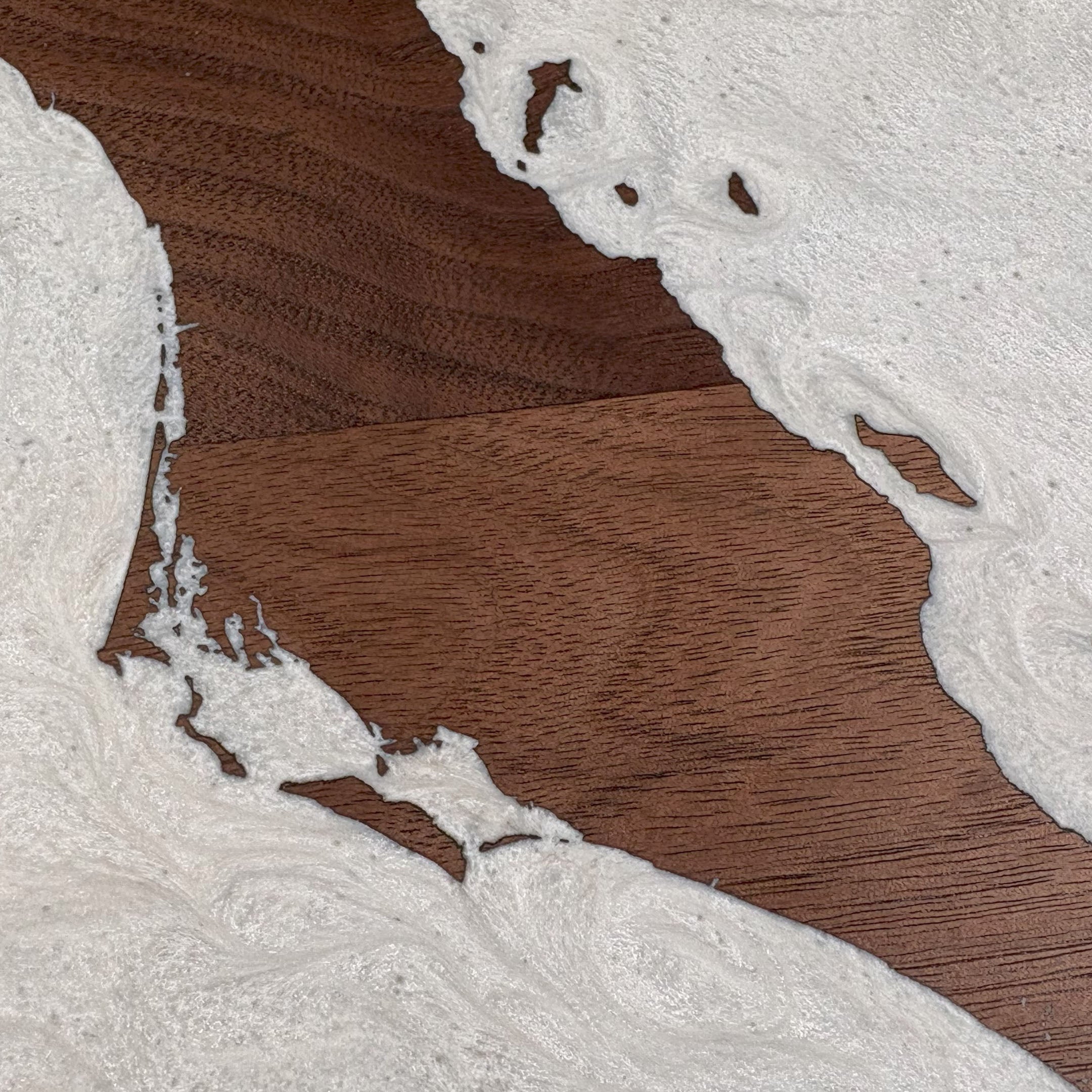 Close-up of custom walnut wood wall art featuring a white resin inlay map design with intricate coastline details, highlighting natural wood grain and texture