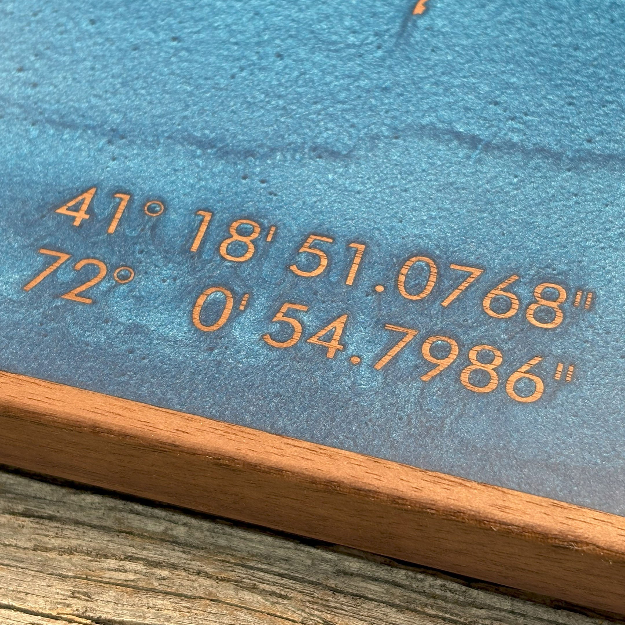 Close-up of custom wall art featuring blue resin art inlay with engraved geographic coordinates, showcasing precision craftsmanship and detailed design