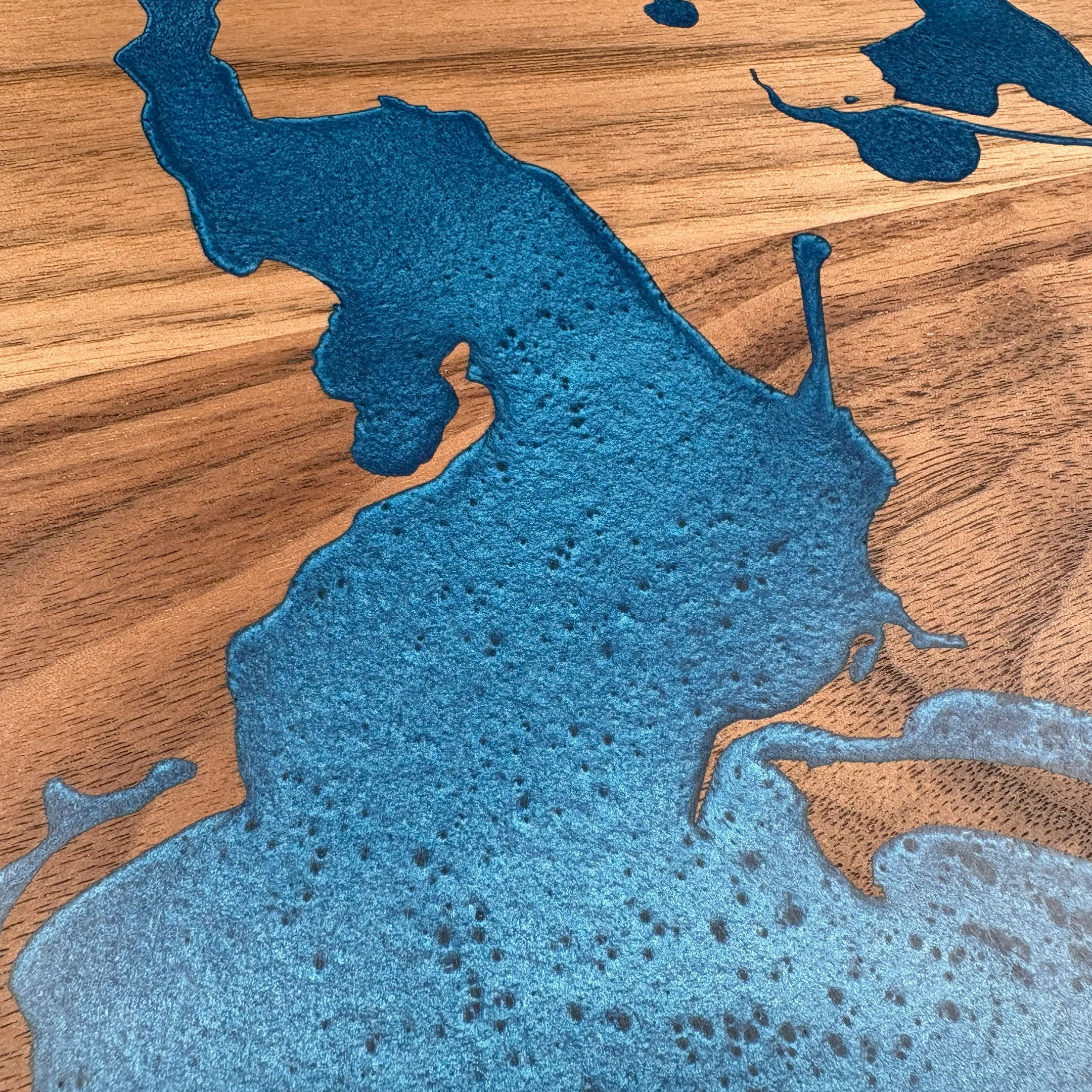 Close-up of custom walnut wood wall art featuring a vibrant blue resin inlay map with detailed textures, highlighting intricate craftsmanship and natural wood grain