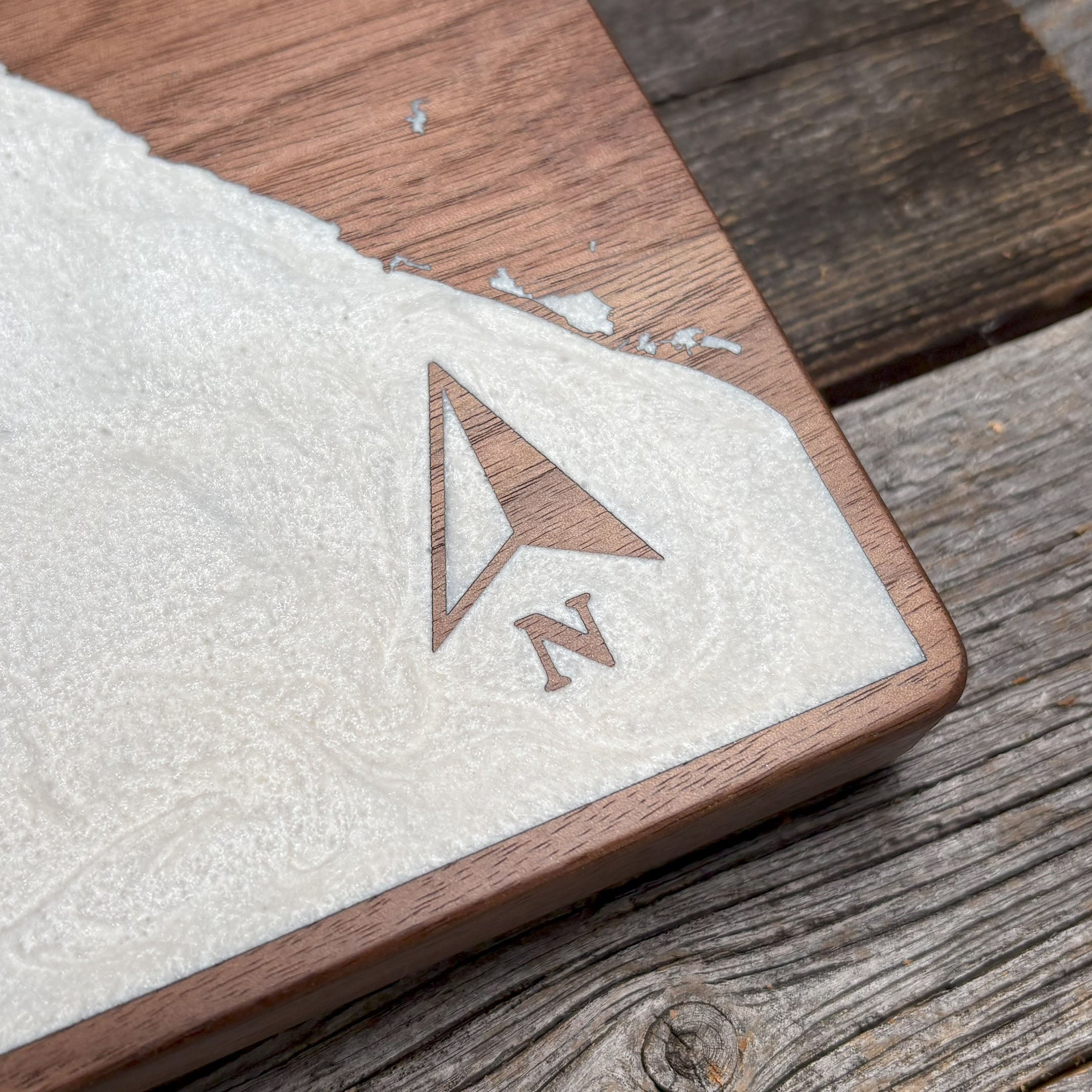 Close-up of custom walnut wood wall art featuring a white resin inlay with an engraved compass arrow pointing north, showcasing detailed craftsmanship and rustic design