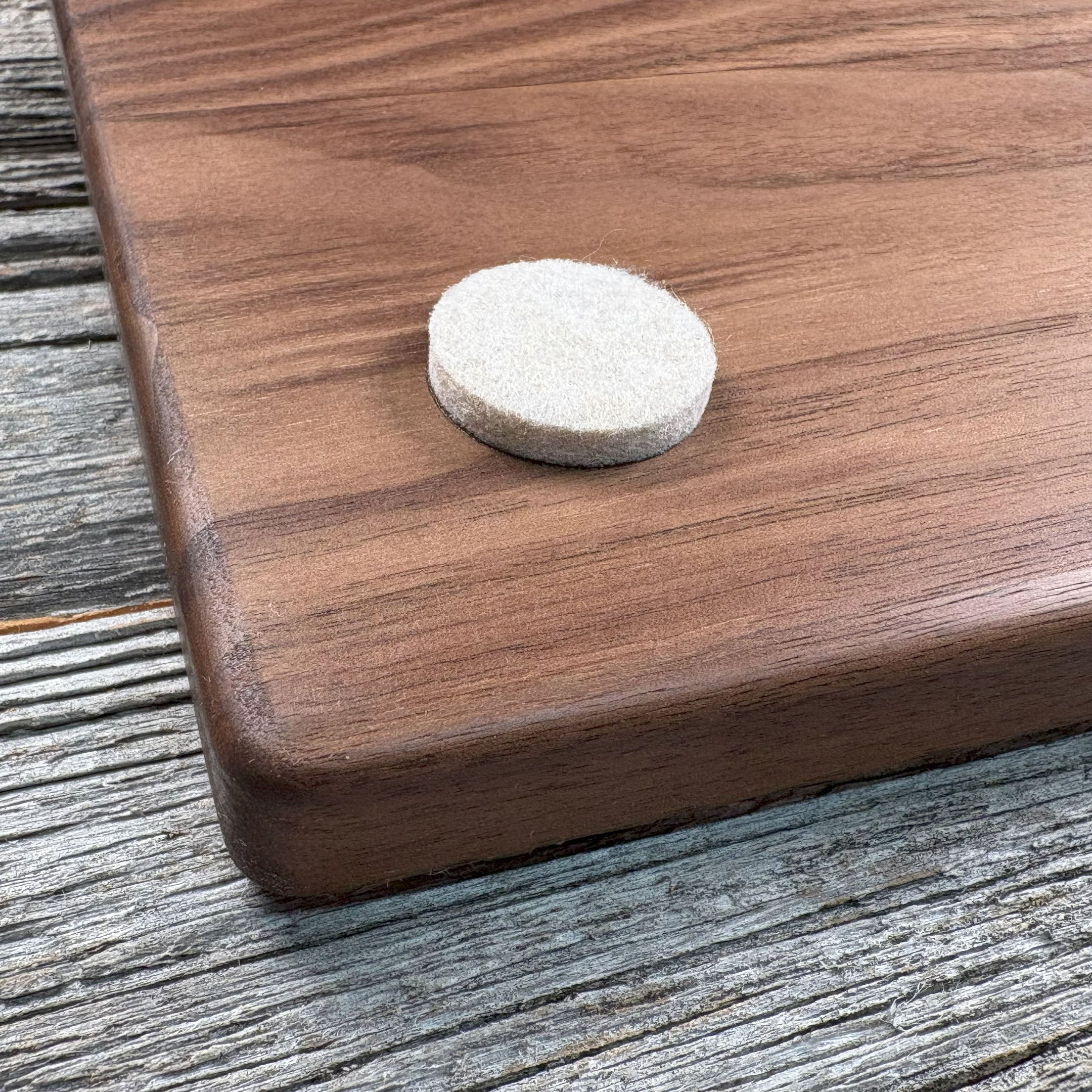 Close-up of a felt pad affixed to the backside corner of custom walnut wood wall art, highlighting protective details and smooth wood craftsmanship