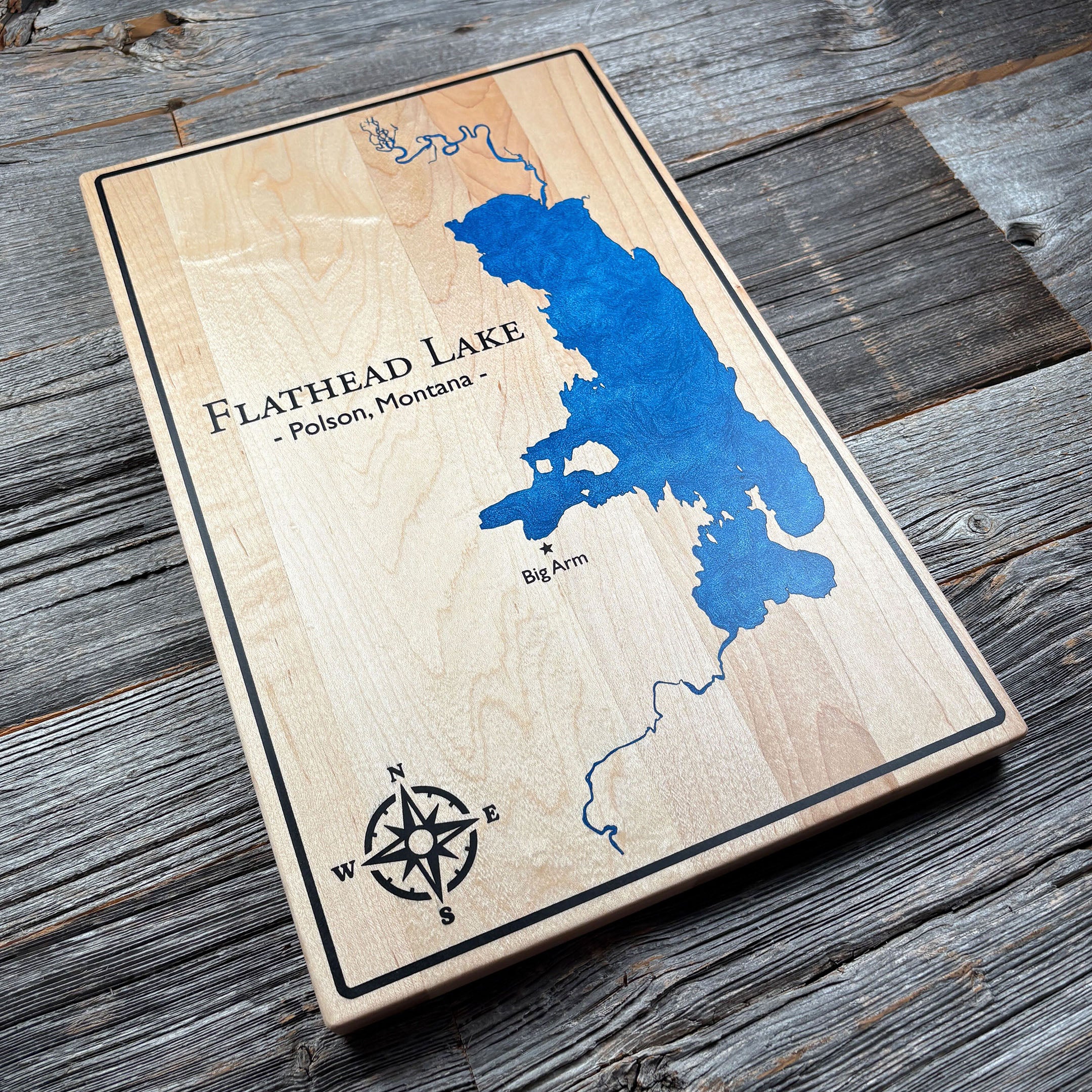 Engraved wooden wall art featuring a blue epoxy resin inlay map of Flathead Lake, Polson, Montana, with a compass rose and 'Big Arm' marked, perfect for personalized décor or gifts.