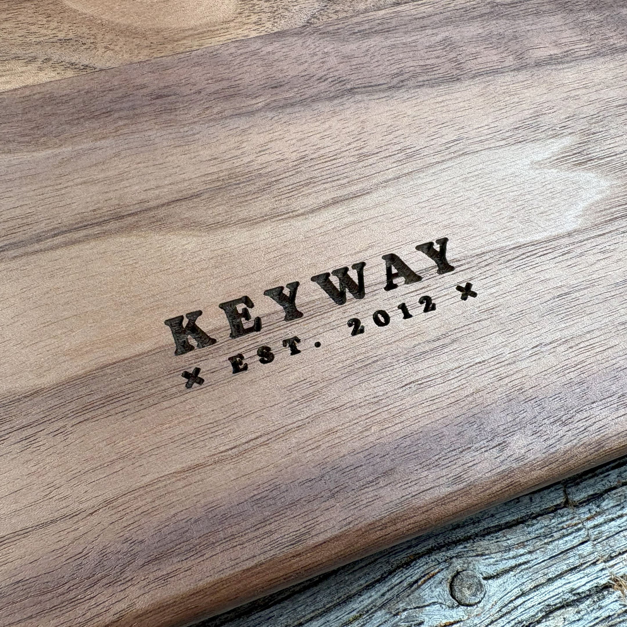 Close-up of the engraved 'Keyway Est. 2012' branding on the backside of custom walnut wood wall art, highlighting detailed craftsmanship and the natural wood grain