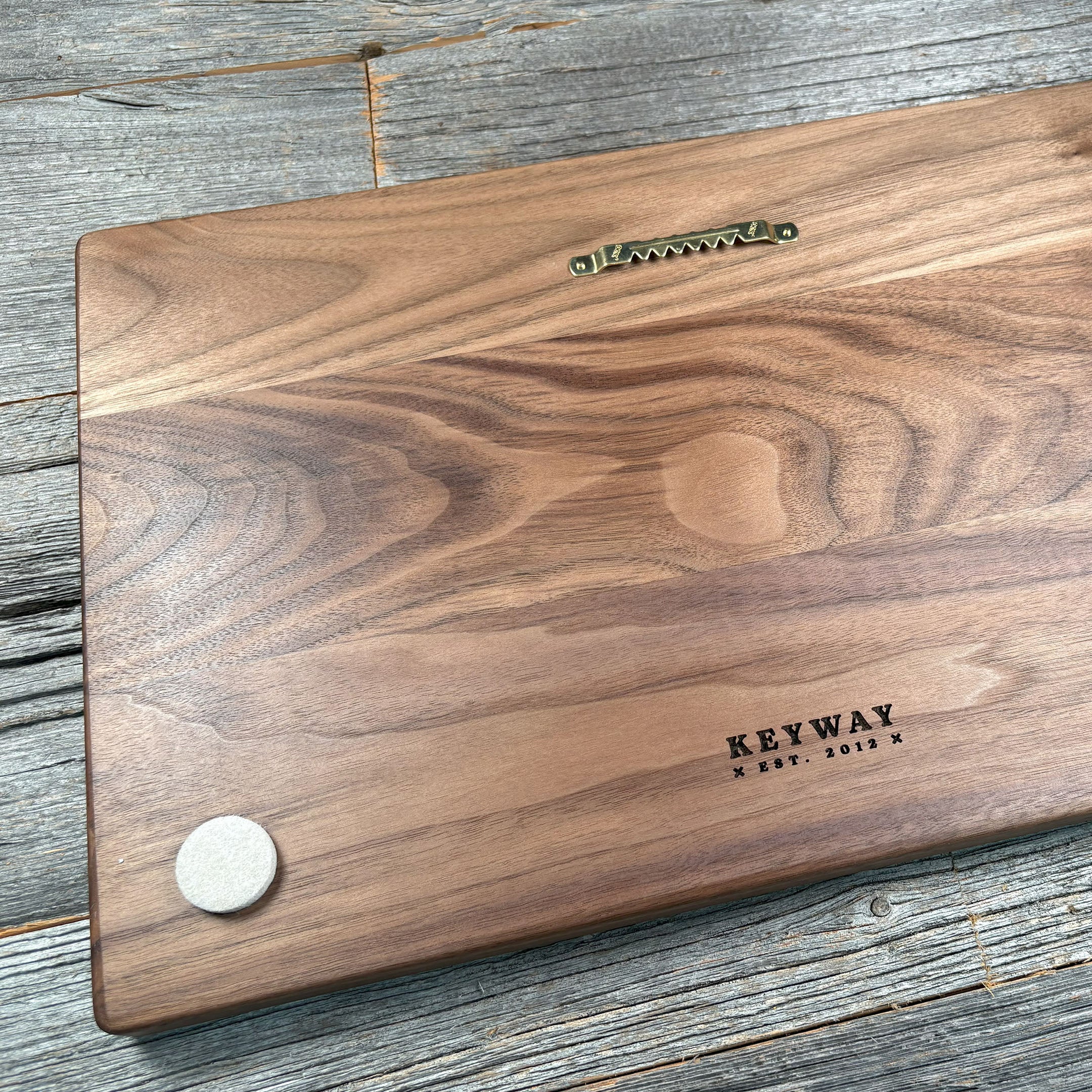 Backside of custom walnut wood wall art featuring a mounted sawtooth hanger and engraved 'Keyway Est. 2012' branding, highlighting the smooth wood grain and craftsmanship