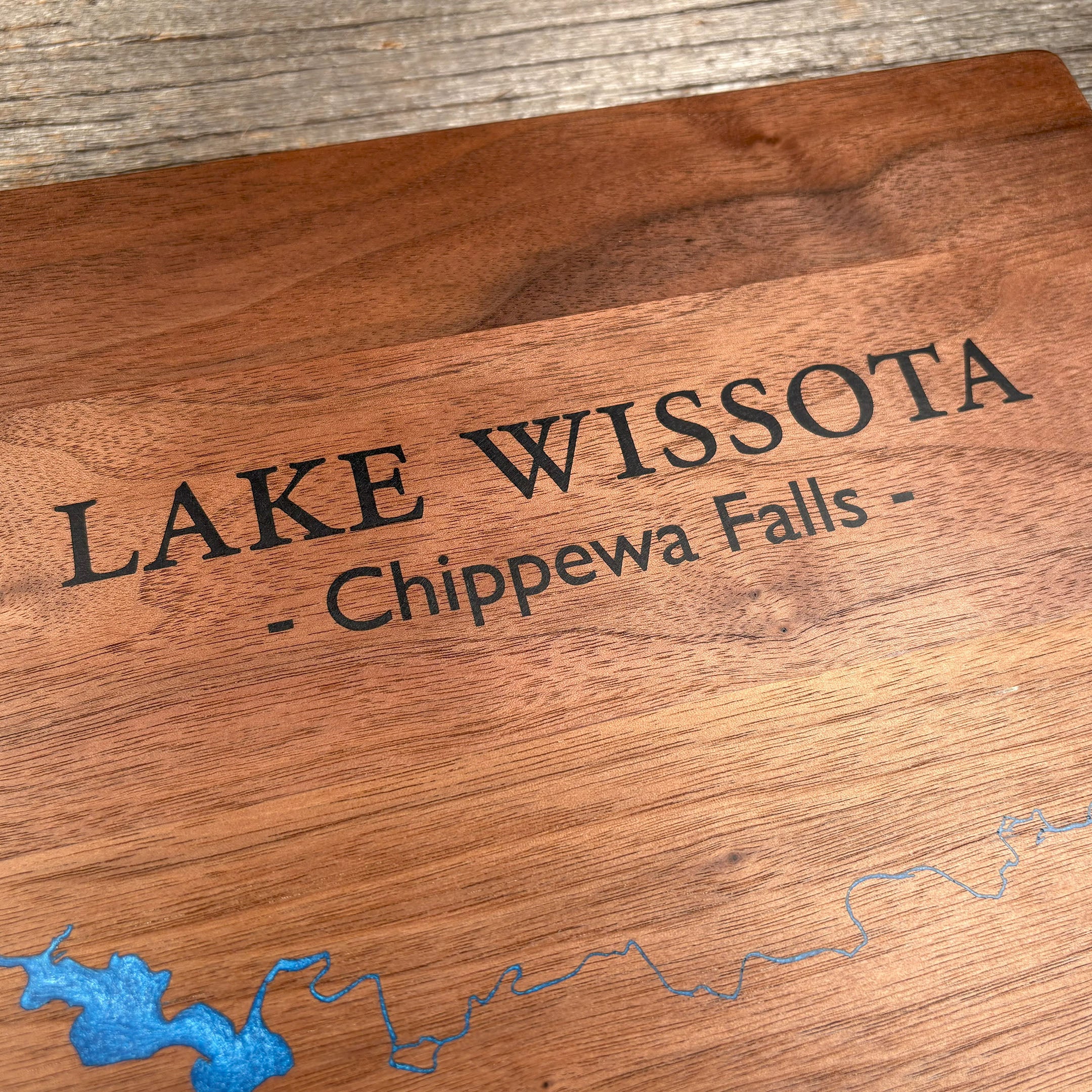 Close-up of custom walnut wood wall art featuring an engraved map of Lake Wissota, Chippewa Falls, with a detailed blue resin inlay and rustic wooden texture