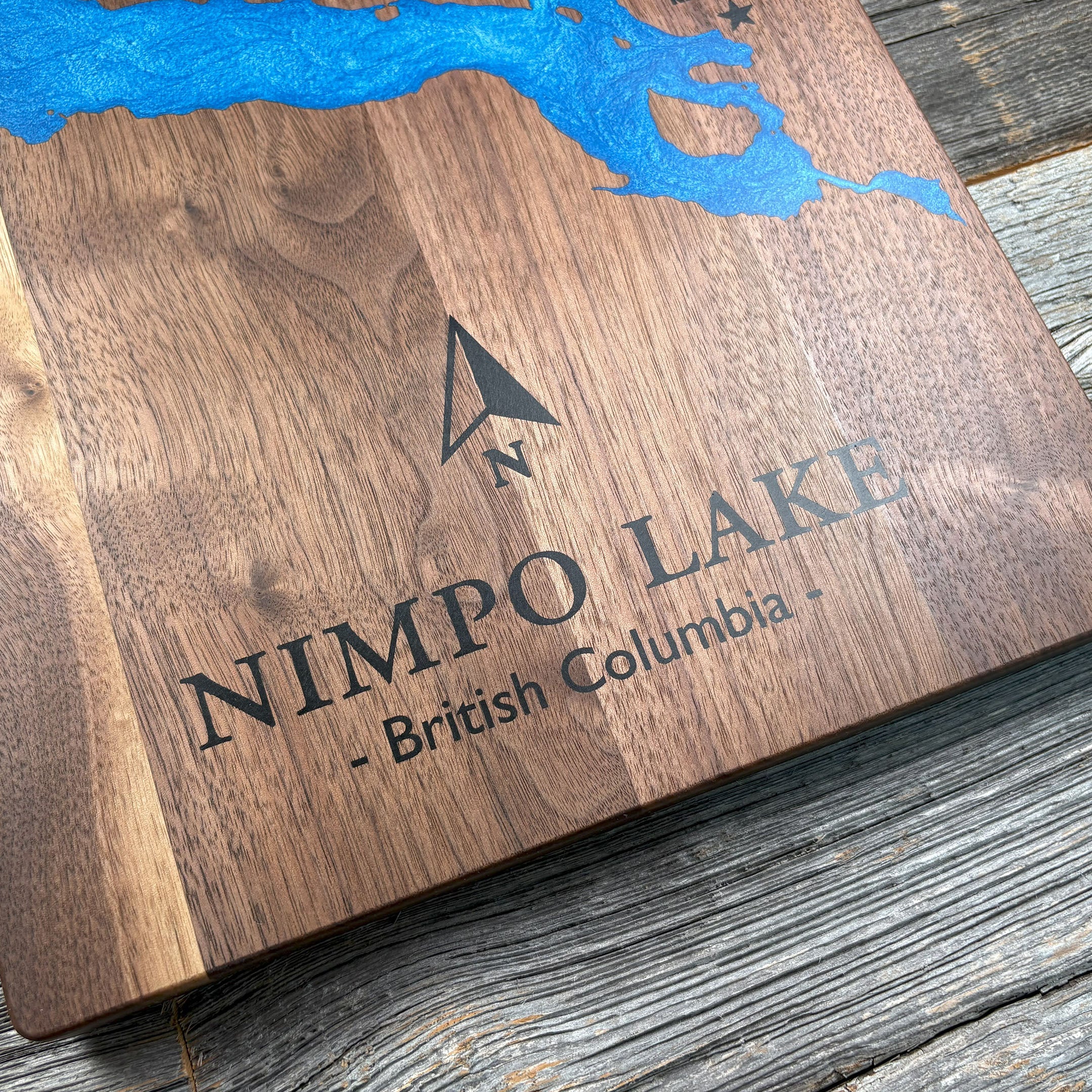 Custom walnut wood wall art featuring a blue resin inlay map of Nimpo Lake, British Columbia, with an engraved compass arrow and text, highlighting natural wood grain and detailed craftsmanship