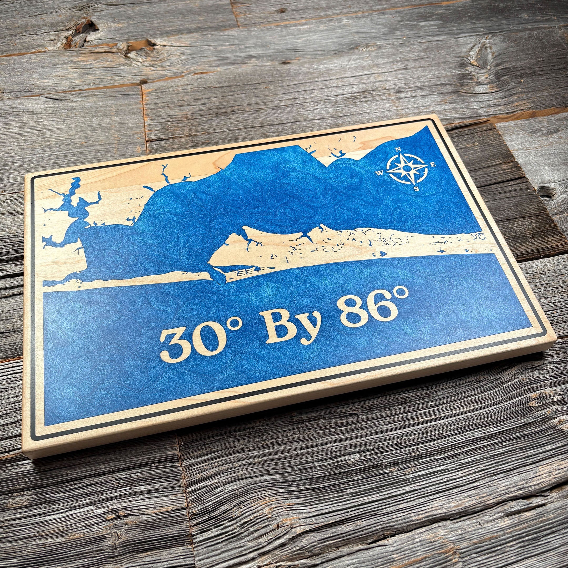 Custom wooden wall art featuring a blue epoxy resin inlay map design with coordinates '30° By 86°' and a compass rose, perfect for personalized home décor.