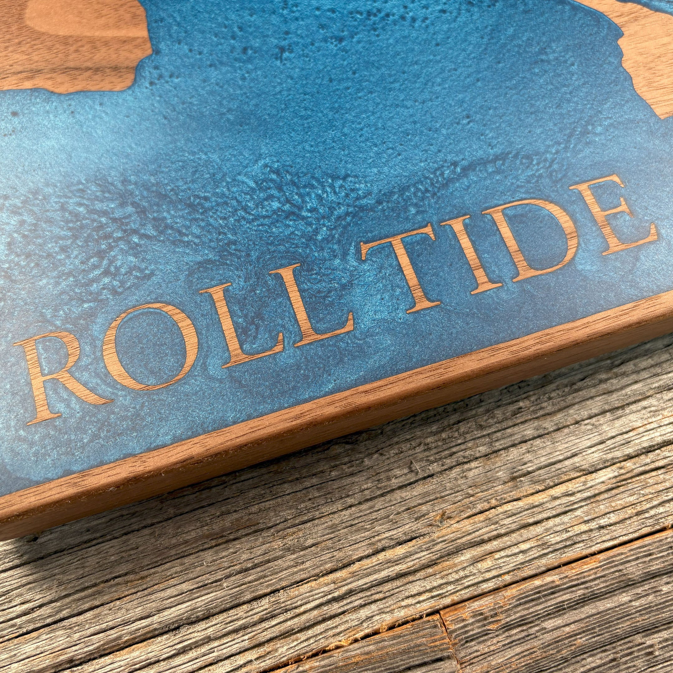 Close-up of custom walnut wood wall art featuring a blue resin inlay and the engraved text 'Roll Tide,' highlighting detailed craftsmanship and vibrant textures