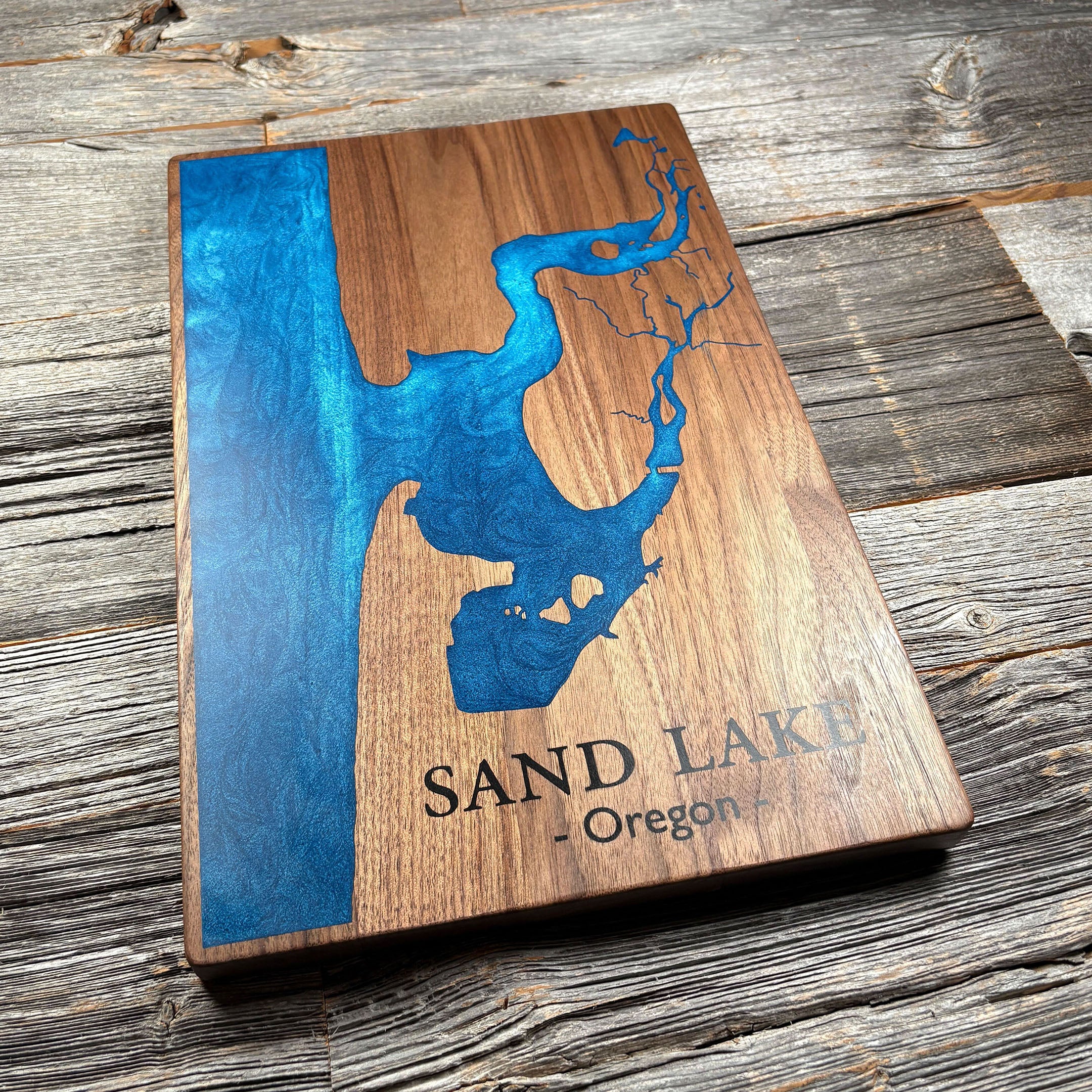 Engraved wooden wall art featuring a blue epoxy resin inlay map of Sand Lake, Oregon, ideal for personalized décor or gifts.