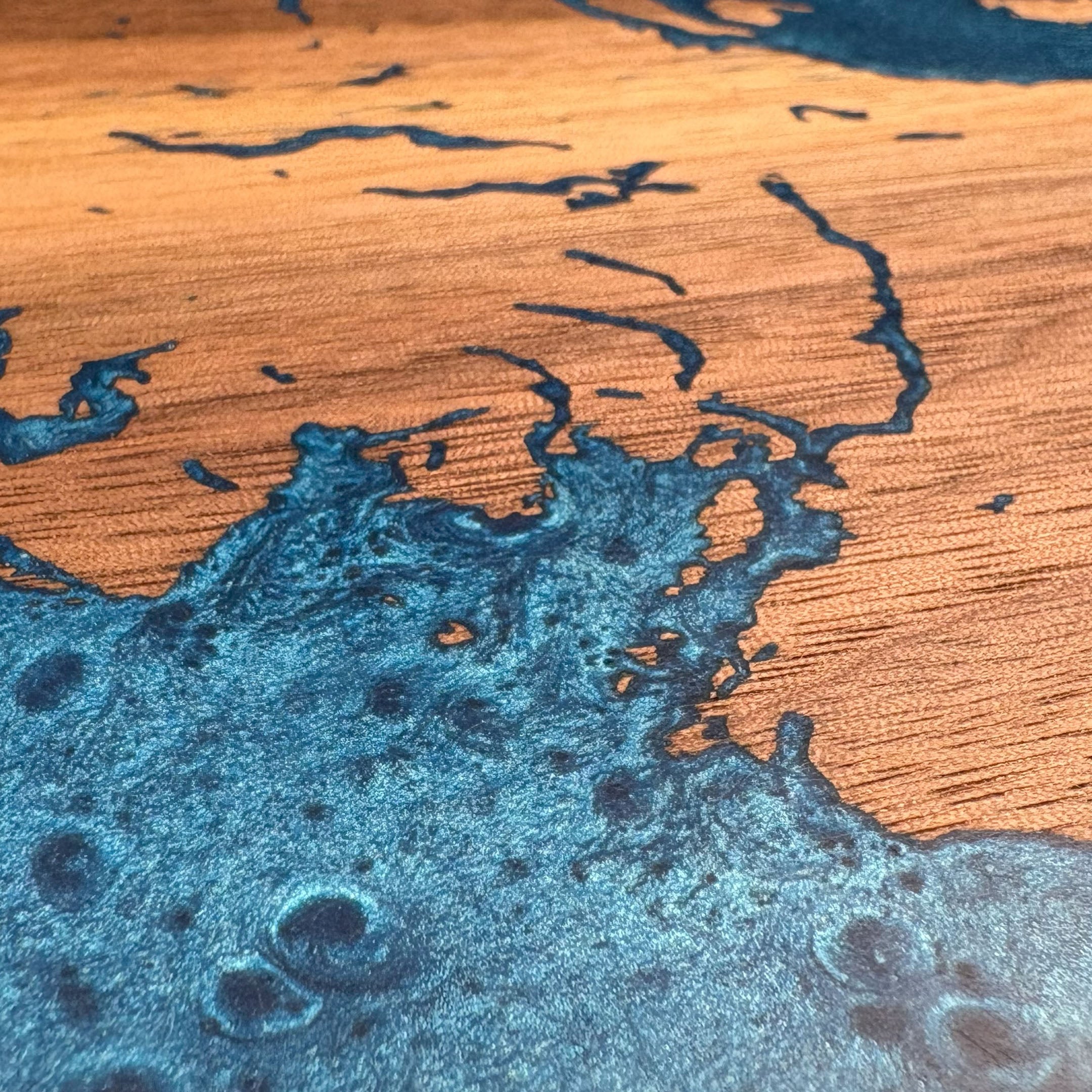 Close-up of custom walnut wood wall art showcasing intricate blue resin inlay detailing waterways with a natural wood grain background