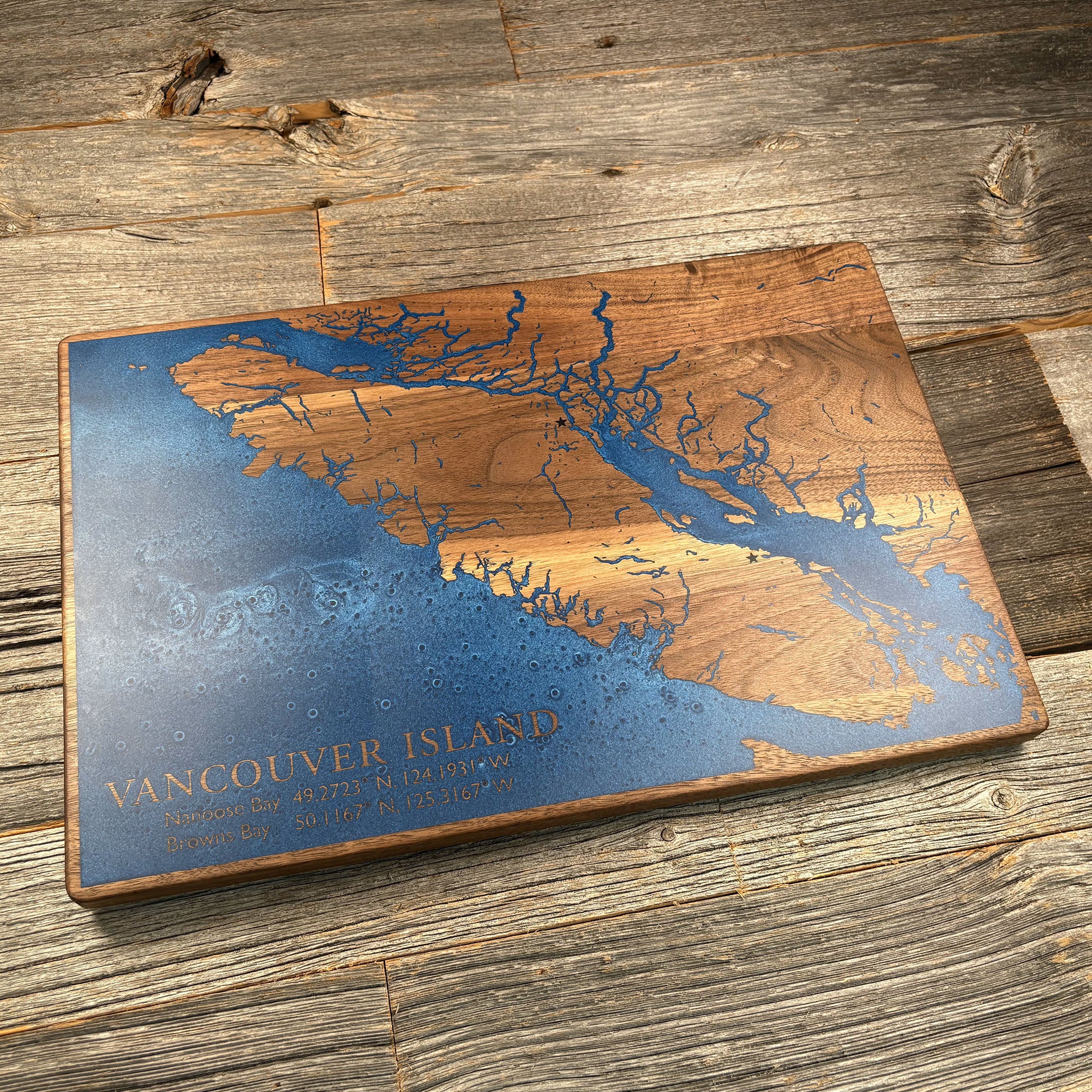 Custom walnut wood wall art featuring a blue resin inlay of Vancouver Island, engraved with coordinates for Nanoose Bay and Browns Bay, displayed on a rustic wooden background