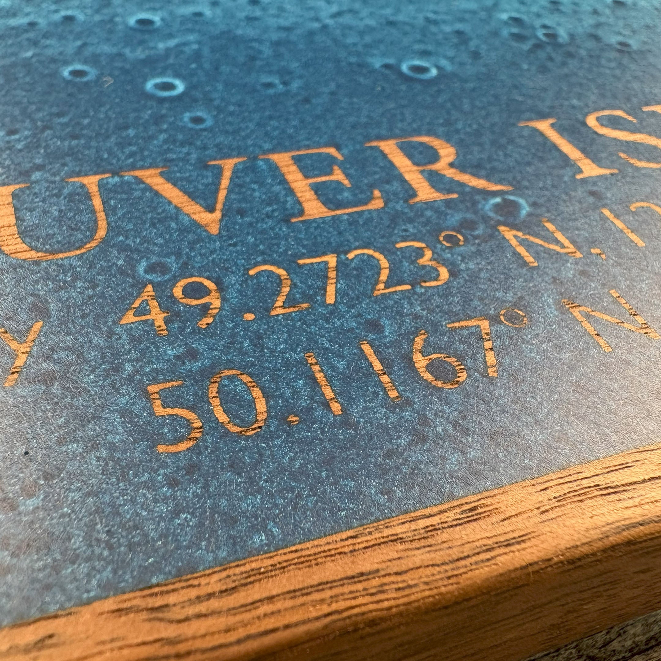 Close-up of custom wall art featuring blue resin art inlay with engraved text highlighting Vancouver Island and detailed coordinates, showcasing intricate craftsmanship and texture